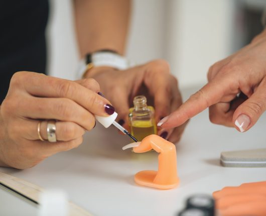 Manicure and nail technician course and training. Beautician applying cuticle oil on nails and fingers